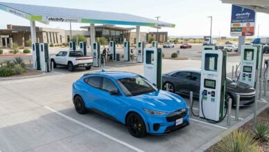 photorealistic image of a Ford Mustang Mach-E charging at a modern, multi-stall Electrify America station at a bright highway rest stop