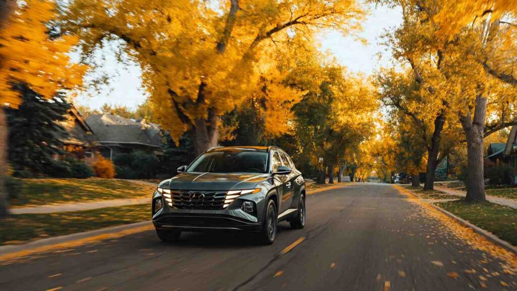 2026 Hyundai Tucson Hybrid driving on a tree-lined suburban road in autumn